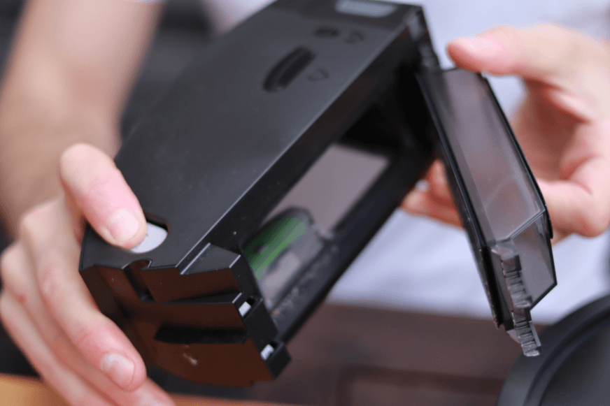 Der mobile Schmutzbehaelter eines iRobot Roomba Saugroboters wird in der Hand gehalten